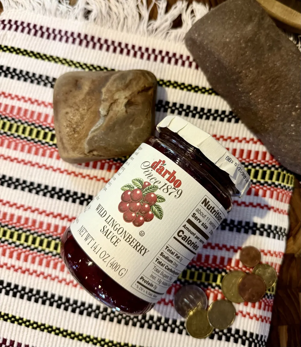 A jar of wild lingonberry sauce with bread rolls on a woven towel